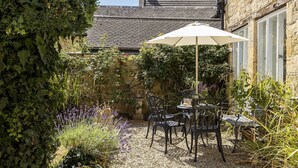Eine Terrasse mit Tisch und Stühlen, umgeben von Pflanzen und einer Steinmauer.