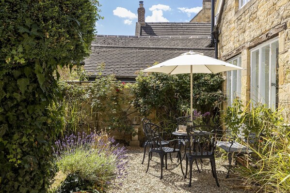 A patio with a table and chairs, surrounded by plants and a stone wall.