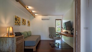 A compact bedroom with a bed, a desk with a computer, a chair, and wall art. - Flow Gili Air (Gili Air)