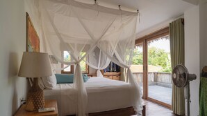 A bedroom with a bed under a canopy, a bedside table with a lamp, a fan, and a view of the outdoors. - Flow Gili Air (Gili Air)