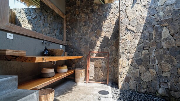 A stone-walled bathroom with a wooden shelf, a mirror, and a small wooden stool. - Flow Gili Air (Gili Air)