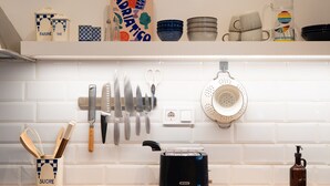 Une cuisine avec un mur recouvert de carreaux blancs, un grille-pain, une passoire et divers ustensiles et plats.