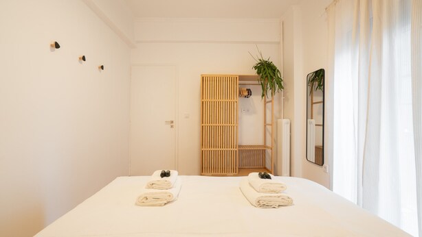 Une chambre d’hôtel avec un lit, des serviettes, un miroir, une plante et une armoire en bois.