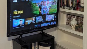 En platt-TV placerad på ett svart stativ med en hylla under.