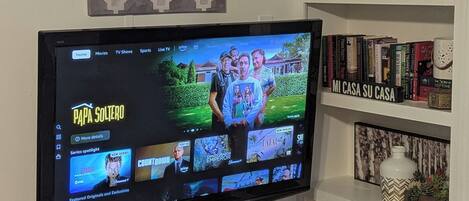 Ein Flachbildfernseher auf einem schwarzen Standfuß mit Ablagefläche darunter.