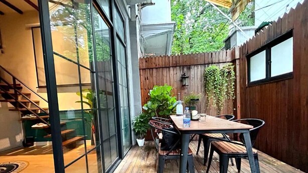 A wooden deck with a table and chairs, a potted plant, and a view of a staircase and greenery. - Shanghai Hills& ZINN city bnb (Shanghai)