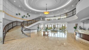 Eine geräumige Lobby mit einer imposanten Treppe, einem Empfangsbereich und einem großen Fenster mit Blick ins Freie.