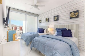 A modern bedroom with two beds, a ceiling fan, and a city view. - Marea | Medano Beach Cabo Luxury Condo Rental (Cabo San Lucas)