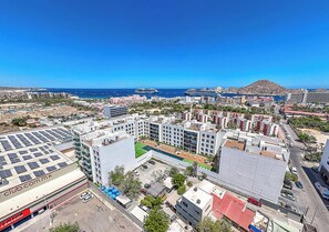 A high-rise hotel with multiple floors, a rooftop pool, and a view of the ocean and distant islands. - Marea | Medano Beach Cabo Luxury Condo Rental (Cabo San Lucas)