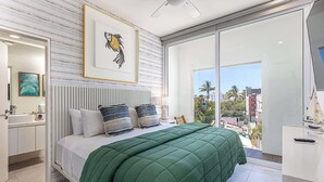 Ein modernes Schlafzimmer mit einem großen Bett, einem Kopfteil, einem Gemälde und Blick auf die Stadt durch große Fenster.
