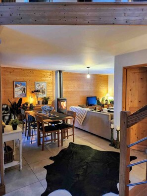 A cozy living room with a fireplace, wooden walls, a dining area, and a sofa. - Chalet Abricotine, sleeps 10, Hot tub (Saint-Jean-d´Aulps)