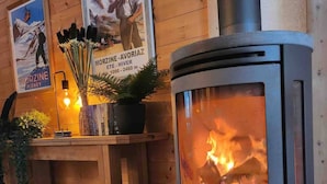 A wood-burning stove in a room with wooden walls, a tiled floor, and a small table with a potted plant and a sign above it. - Chalet Abricotine, sleeps 10, Hot tub (Saint-Jean-d´Aulps)