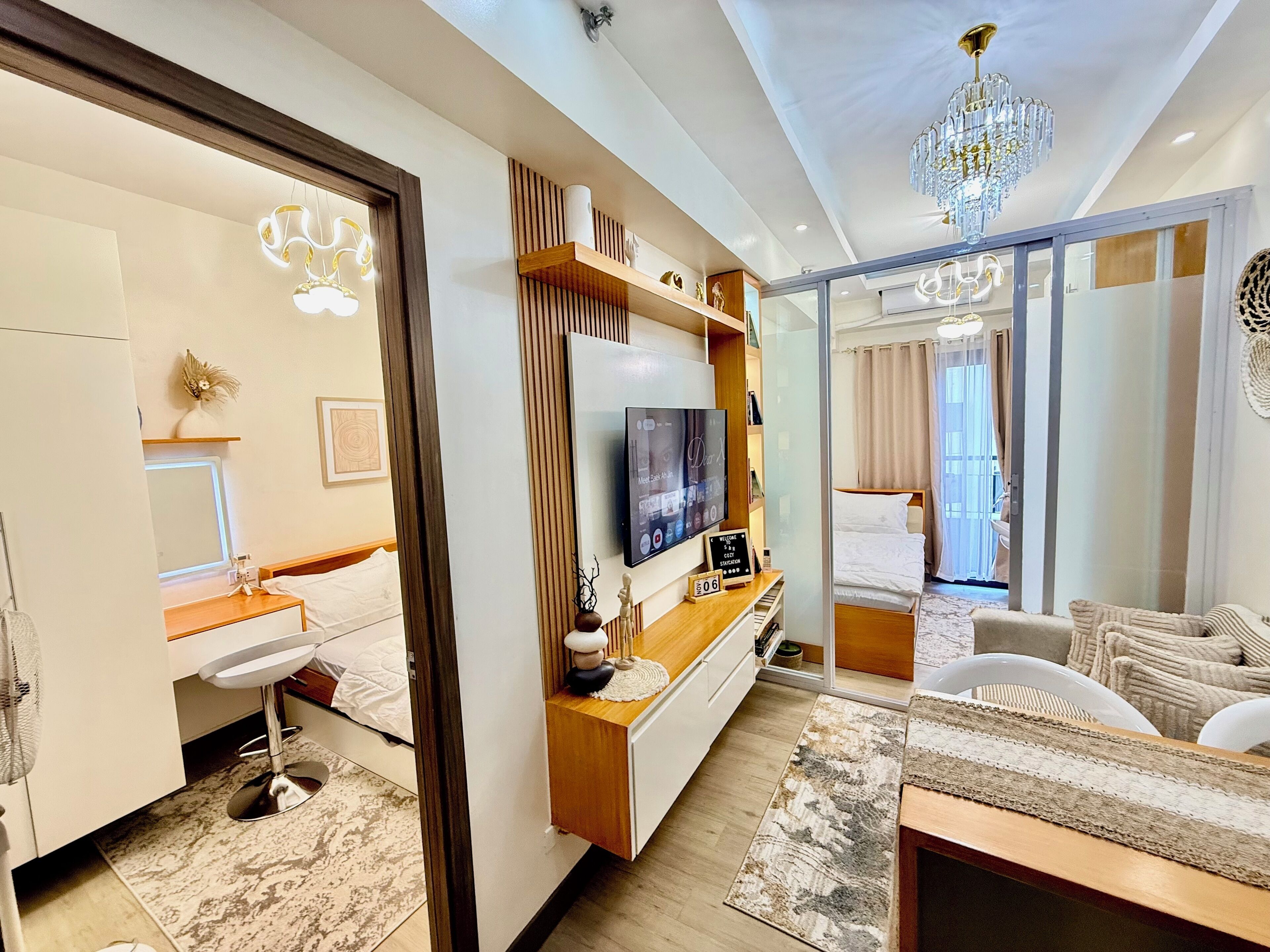 A modern hotel room with a large bed, a sitting area with a sofa, a TV, and a chandelier.