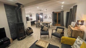 A living room with a fireplace, sofa, coffee table, and a dining area with a table and chairs. - Chalet Clocher Sleeps 10 Hot tub (Essert-Romand)