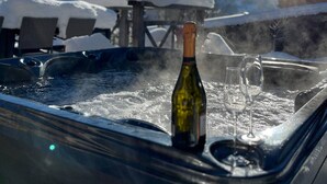 A hot tub with a bottle and glasses, surrounded by snow-covered chairs and a mountain view. - Chalet Clocher Sleeps 10 Hot tub (Essert-Romand)