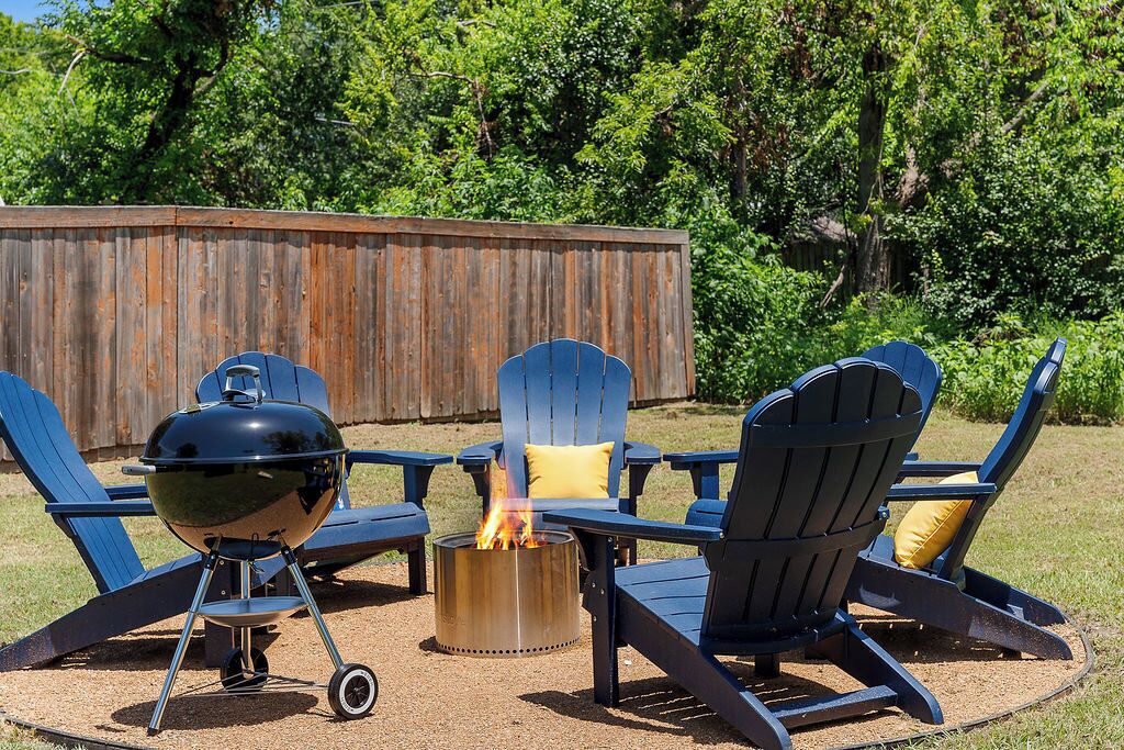 Un espace barbecue comprenant un gril, un foyer et trois fauteuils Adirondack avec coussins.