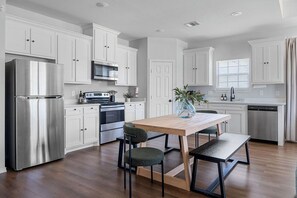 A modern kitchen with white cabinets, stainless steel appliances, and a wooden dining table with chairs. - Family Fun Getaway| Game Room| Fire Pit| Mini Golf (Bonham)