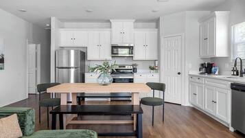 A modern kitchen with white cabinets, stainless steel appliances, and a wooden dining table with four chairs.