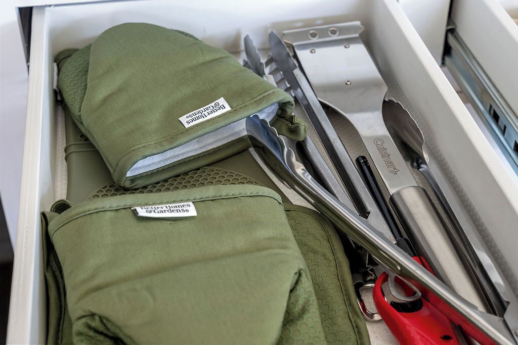 A drawer containing a green bag with a label, a pair of red scissors, and a kitchen utensil.