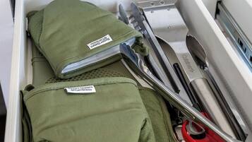 A drawer containing a green bag with a label, a pair of red scissors, and a kitchen utensil.