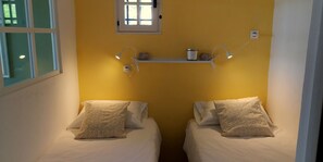 A room with two beds, a shelf with a candle and a small container, and a window with blinds. - Provencal house with sea view La Croix Valmer "Lou Mamet", ideal for families (La Croix-Valmer)
