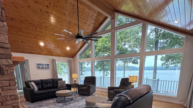 Amplia sala de estar con piso de madera, chimenea de piedra y grandes ventanales con vistas al lago.