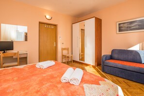 A hotel room with a bed, a desk, a chair, a wardrobe, and a sofa.