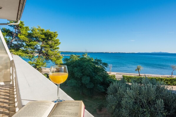 A balcony with a view of the sea, a glass of orange juice, and an open book.