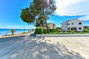A coastal road with a white building, trees, and a clear blue sky.