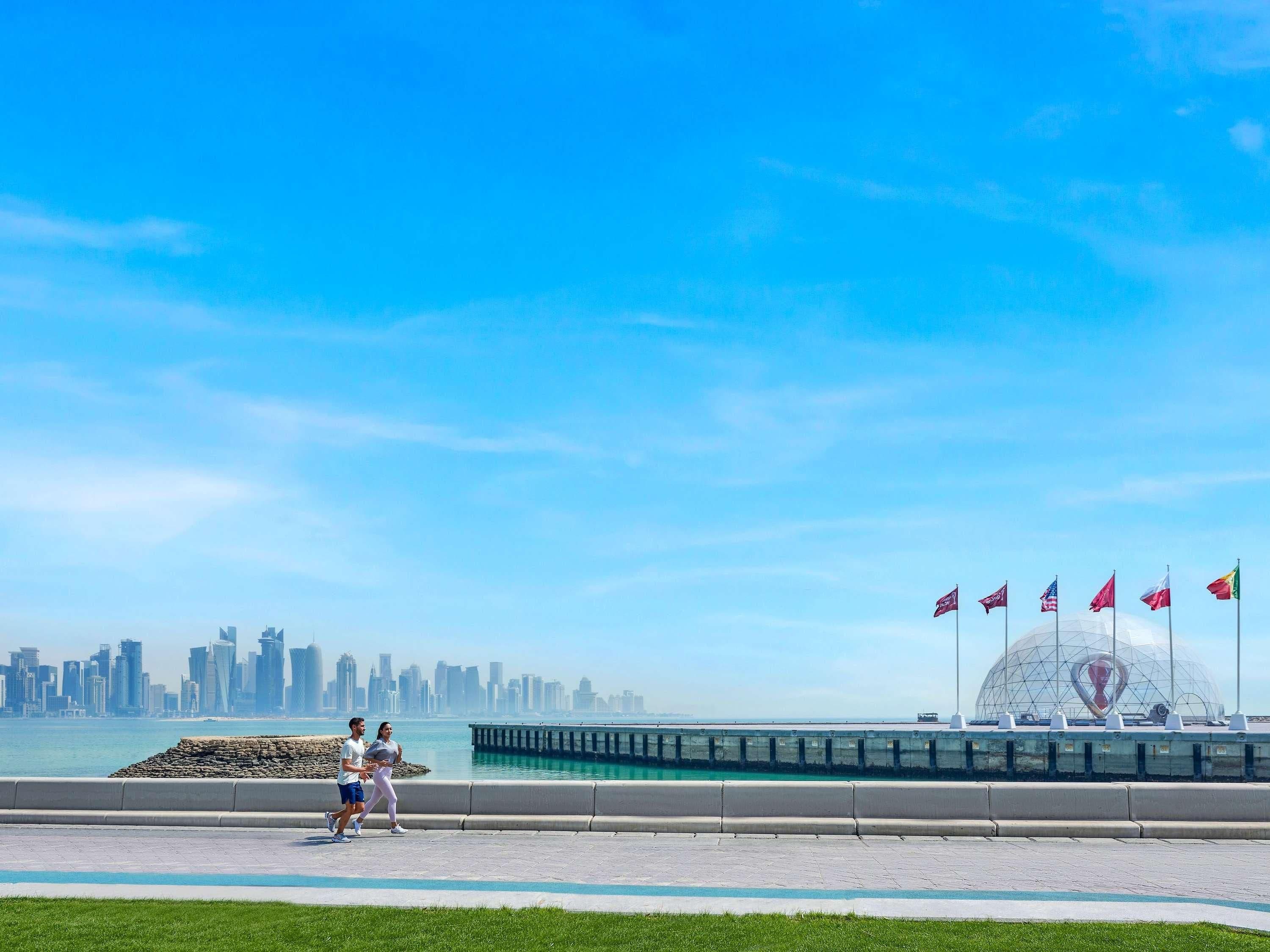 Un paseo marítimo con el horizonte de una ciudad de fondo, una gran estructura en forma de cúpula transparente y varias banderas.