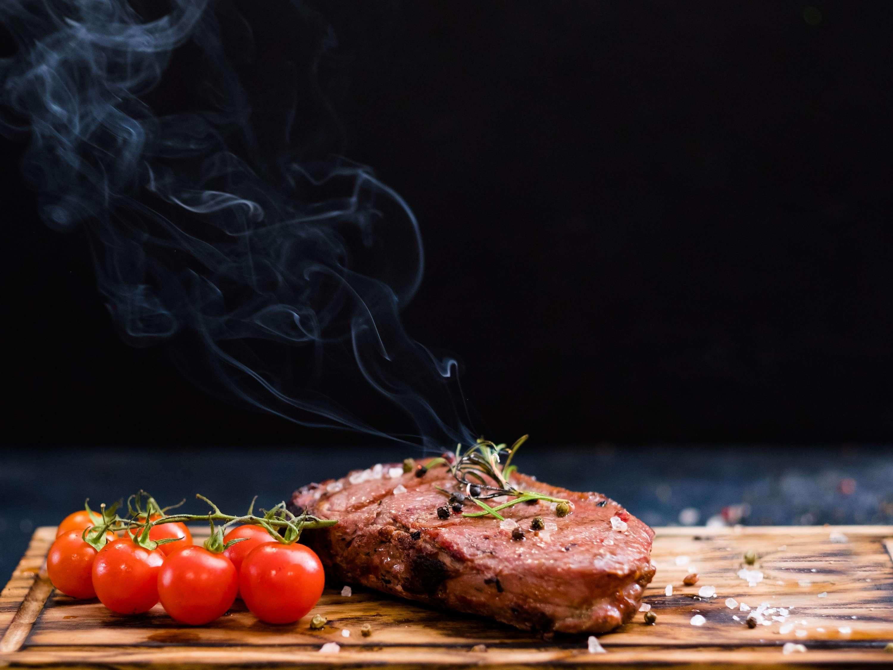 Bife com tomate cereja e ervas sobre uma tábua de madeira.