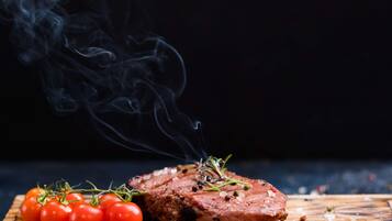Bife com tomate cereja e ervas sobre uma tábua de madeira.
