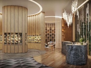 Un intérieur moderne avec une structure en bois aux lignes courbes, où sont exposées des bouteilles, un espace salon avec un canapé et un comptoir d’accueil en pierre.