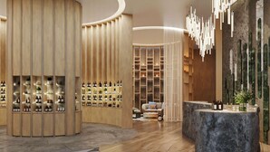 Un intérieur moderne avec une structure en bois aux lignes courbes, où sont exposées des bouteilles, un espace salon avec un canapé et un comptoir d’accueil en pierre.