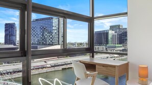 A modern office space with a large window, a desk, a chair, and a lamp.