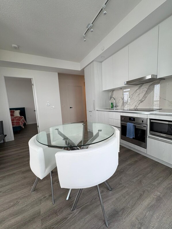 A modern kitchen with white cabinets, a glass dining table, and stainless steel appliances.
