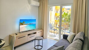 Un salon moderne doté d’un téléviseur à écran plat, d’un canapé, d’une petite table ronde et d’un balcon aménagé avec du mobilier d’extérieur.