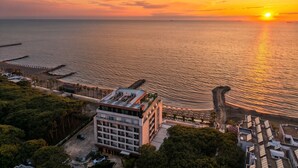 Un hôtel situé sur la côte, offrant une vue sur le coucher de soleil en mer, avec un espace de stationnement et un bâtiment à plusieurs étages.