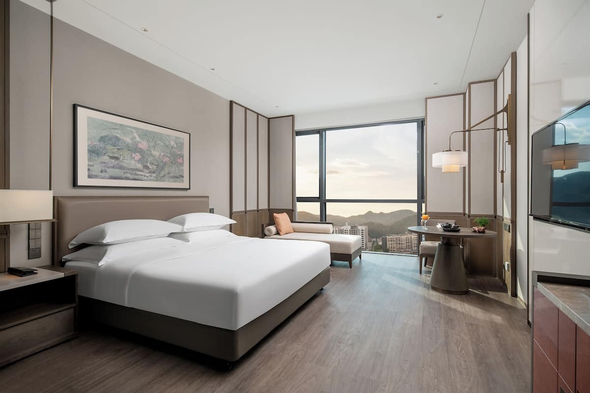 Une chambre d’hôtel moderne dotée d’un grand lit, d’un bureau, d’un canapé, d’une table à manger et d’une grande fenêtre donnant sur la ville.
