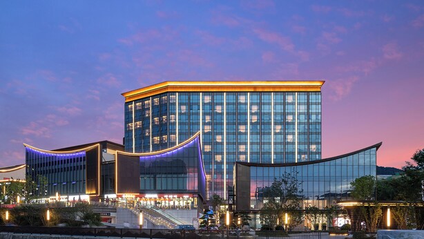 A modern building with a glass facade, a curved entrance, and a staircase leading to the entrance. - Juntels Panan Jinhua (Jinhua)