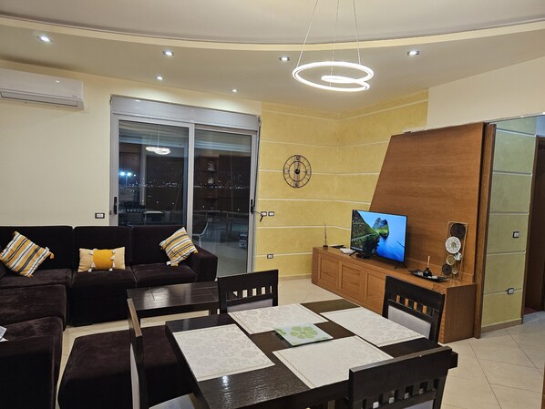A living room with a sofa, coffee table, TV, and a dining area with chairs and a table.