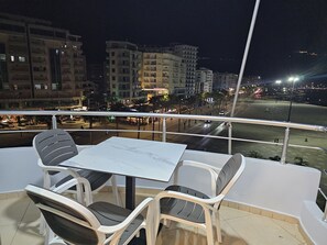 A balcony with a table and chairs, overlooking a cityscape at night. - Holiday Apartment Sea View two Bedroom (Vlorë)