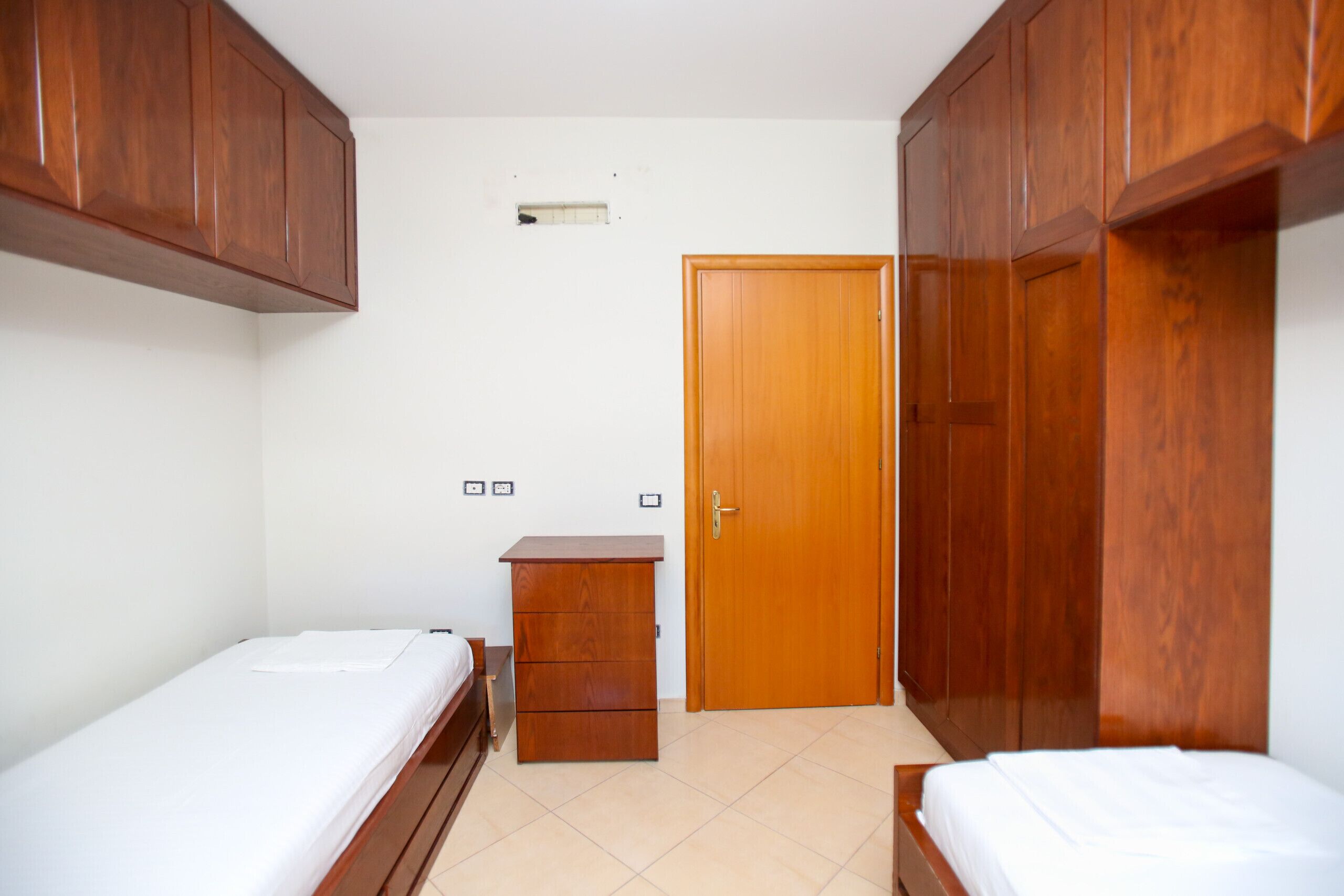 A bedroom with two beds, wooden wardrobes, a small dresser, and a door.
