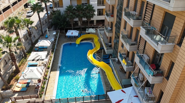 A rooftop pool with a yellow slide, surrounded by lounge chairs and umbrellas.