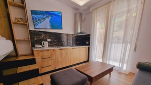 A modern room with a wooden kitchenette, a flat-screen TV, a sofa, and a dining table. - Teo Deluxe Studios - Family Triple  Studio (Vlorë)