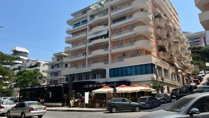 A multi-story hotel with balconies, a ground-level restaurant, and parked cars. - Teo Deluxe Studios - Family Triple  Studio (Vlorë)