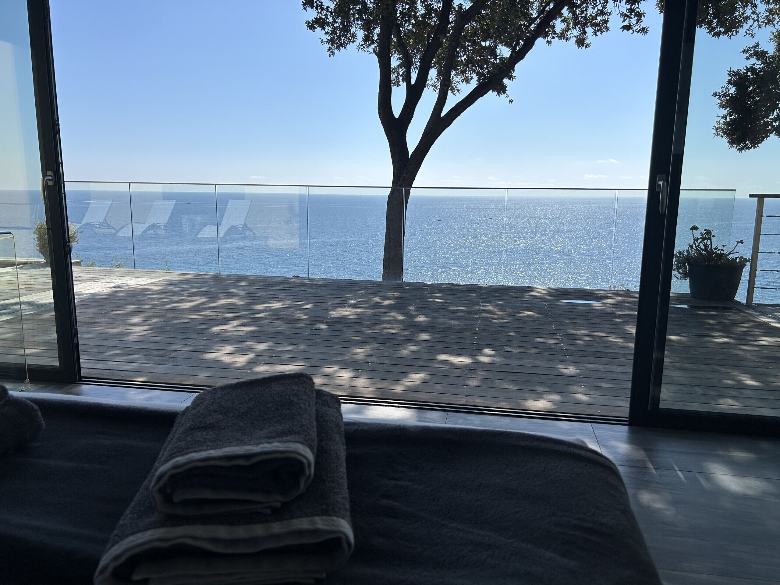 A room with a view of the sea, a wooden deck outside, and a towel on the bed.