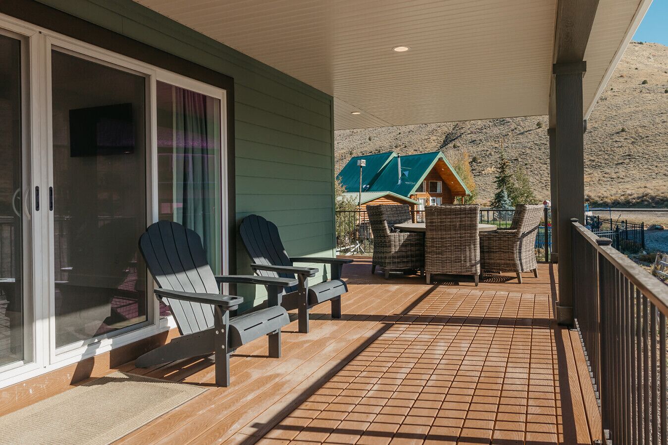 A covered outdoor area with two Adirondack chairs, a small table, and a wicker chair.