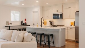 A modern kitchen with a central island, bar stools, white cabinetry, and stainless steel appliances. - Lakeview Lodge - Lakeside Escape (Scofield)