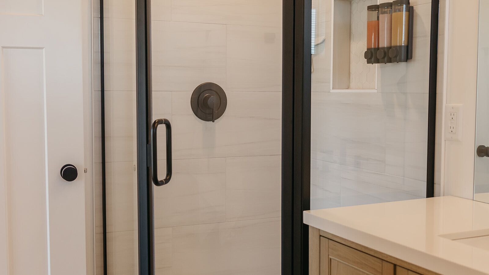 A modern bathroom with a glass shower door, a white tiled wall, and a wooden cabinet.